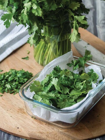 Small container of cilantro on the table with a pile of chopped next to it.