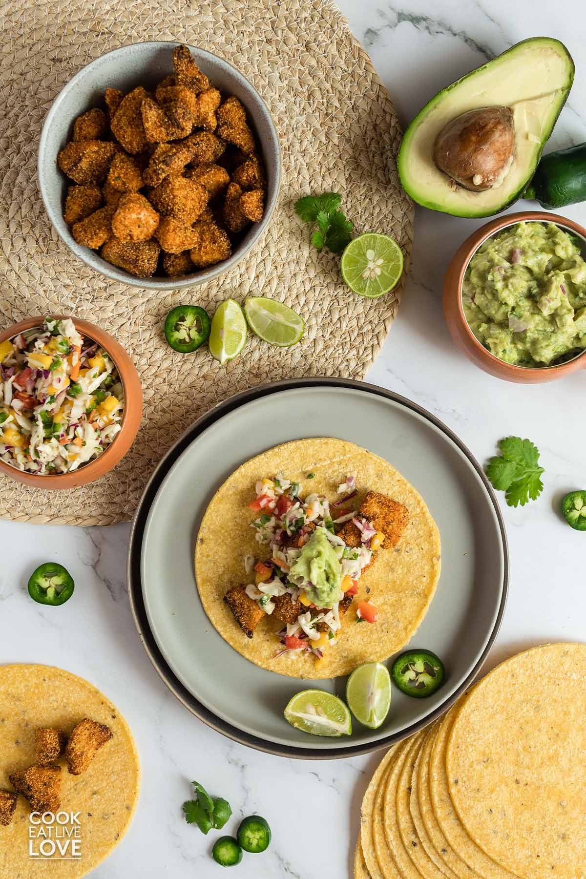 Vegan fish tacos served up on a table with guacamole and jalapenos.