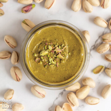 Pistachio butter on the table surrounded by whole and shelled pistachios