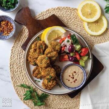 Air fryer falafel served up on a plate with salad, lemons and tahini sauce.