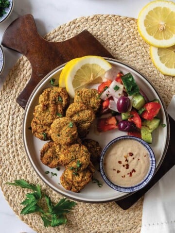 Air fryer falafel served up on a plate with salad, lemons and tahini sauce.