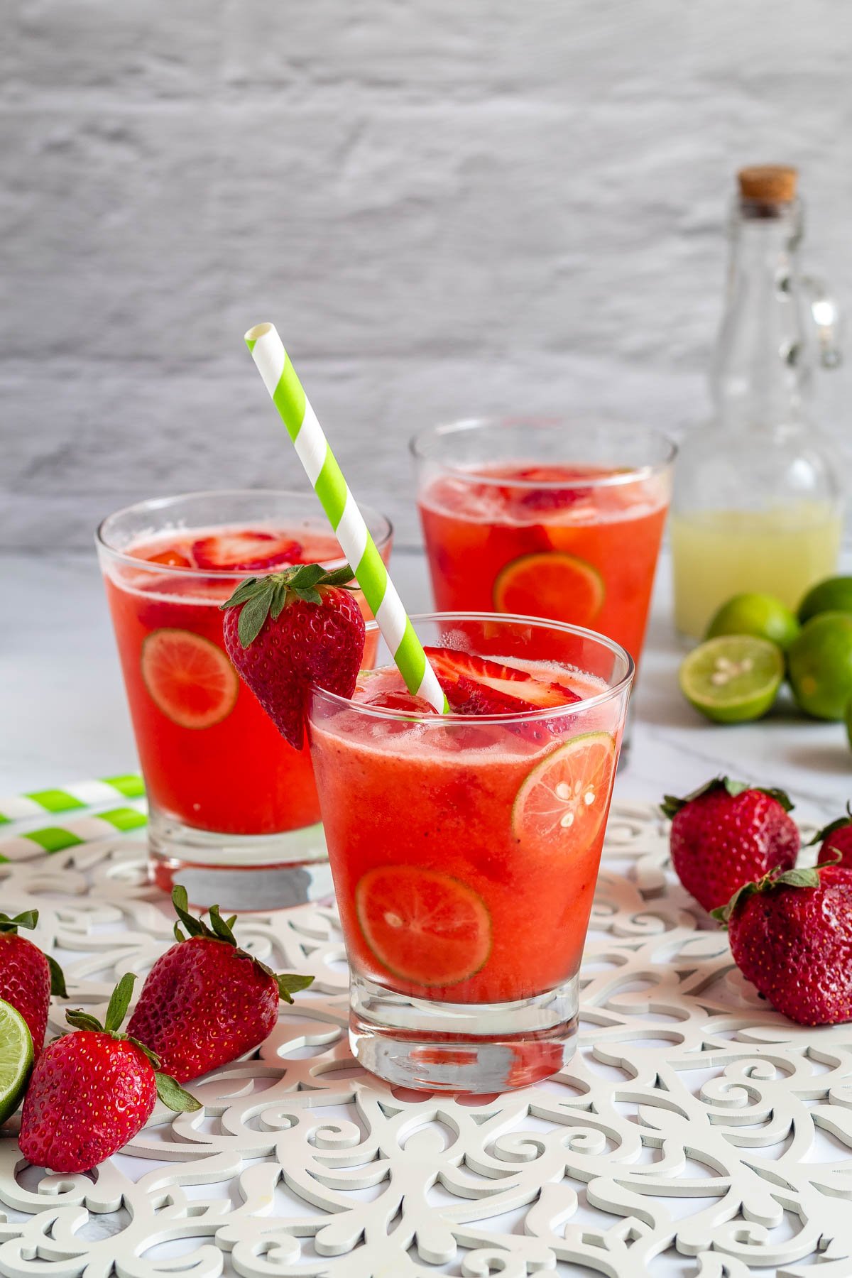 Strawberry limemade poured up into three glasses with a straw in the front glass.