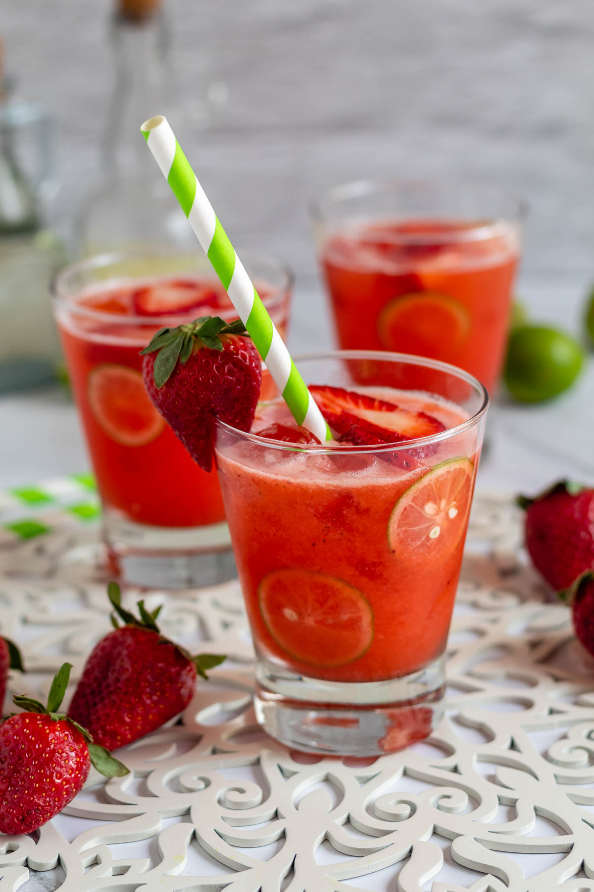 Three glasses of strawberry limemade served up on white table.