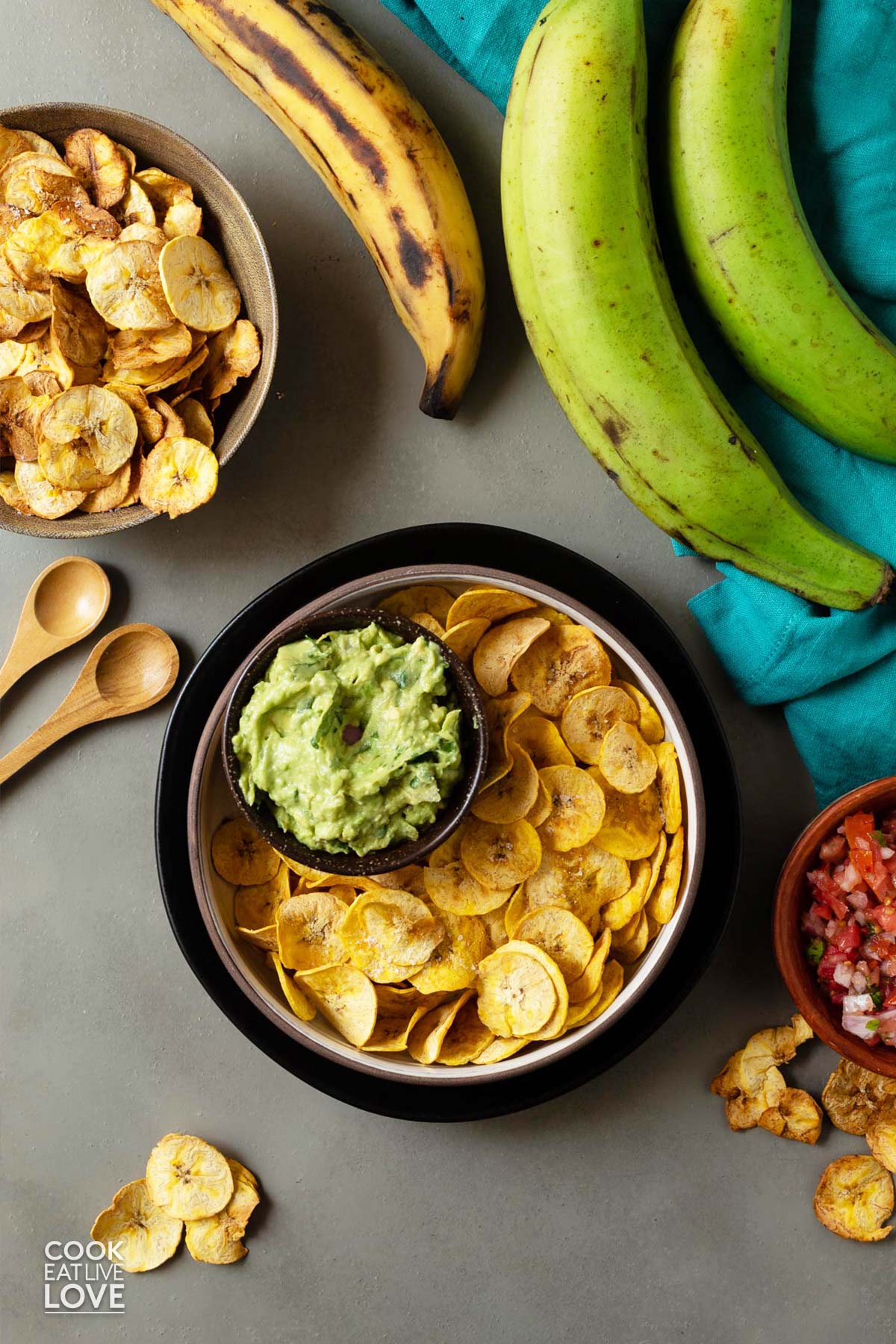 Bowl of plantain chips on the table with green plantains, guacamole and pico de gallo.