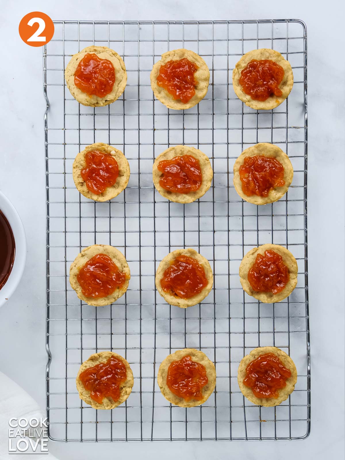Jaffa cakes cooling on wire rack with orange marmalade on top.