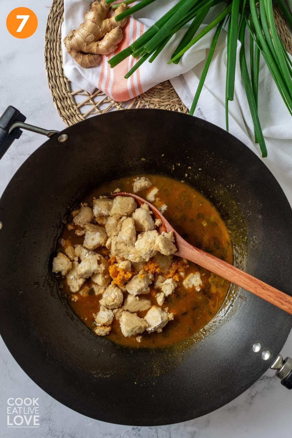 Tofu added to the orange sauce in the wok.