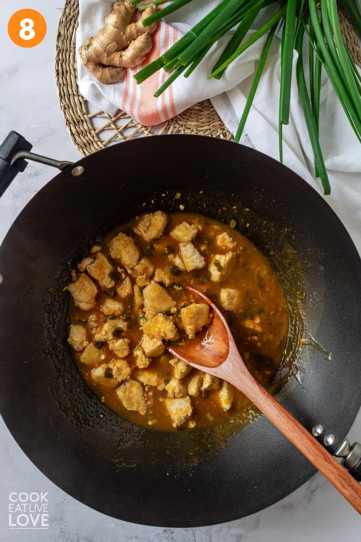 Tofu cooked in orange sauce with wooden spoon in a wok.