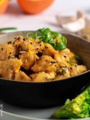 A bowl of crispy orange tofu garnished with green onions and a side of broccoli.