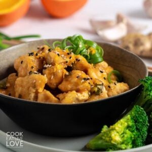 A bowl of crispy orange tofu garnished with green onions and a side of broccoli.