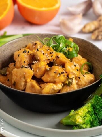 A bowl of orange tofu recipe with green onion curls on top and broccoli on the side.