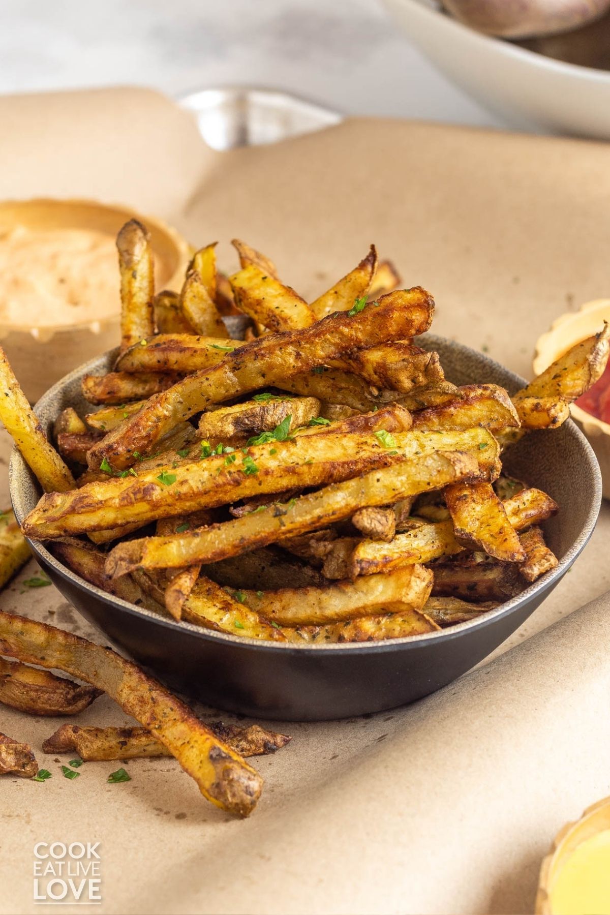 A bowl of oven french fries with dipping sauces. 