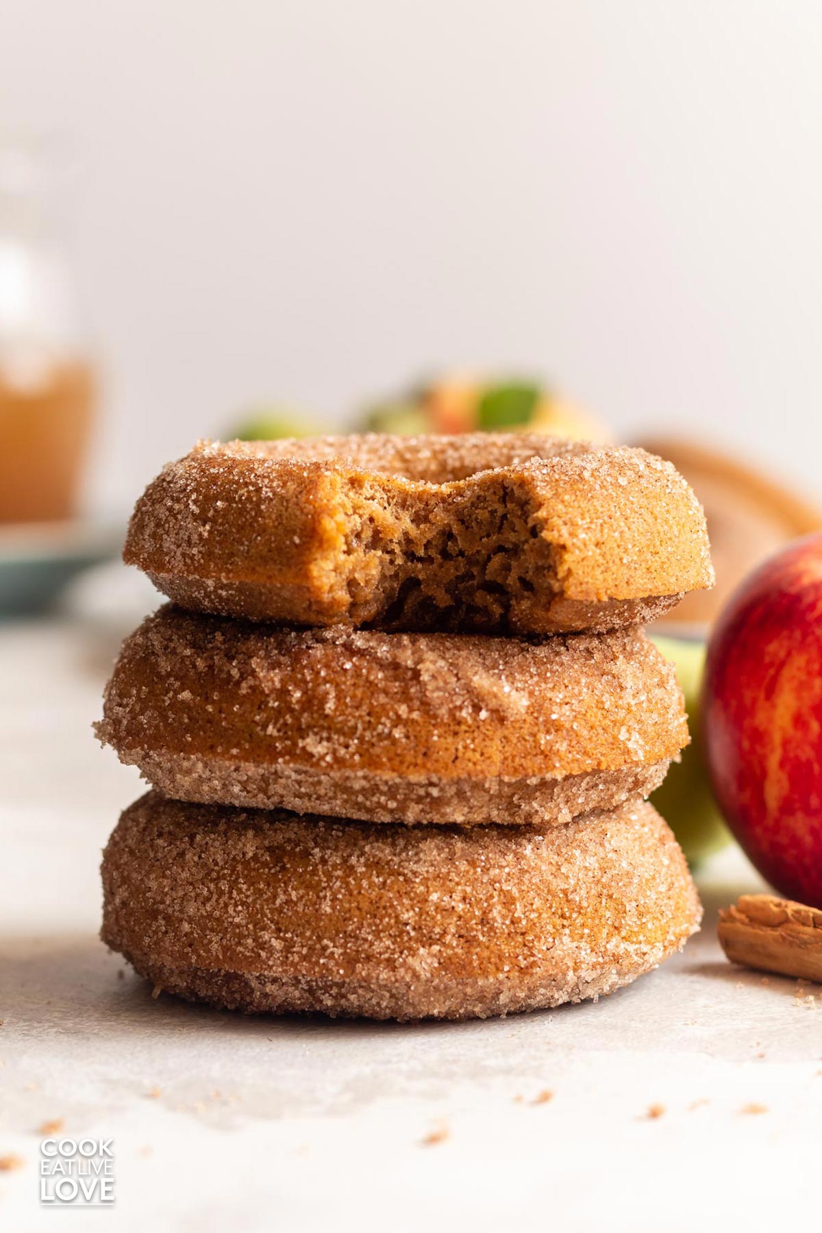 Three vegan apple cider doughnuts in a stack with one missing a bite.