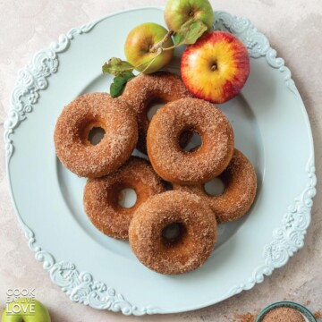 Vegan apple cider doughnuts on a platter with a red and green apple to the side.