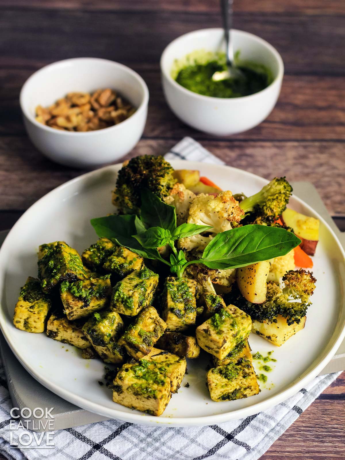 Tofu with pesto on a plate with pesto sauce and walnuts in the back.