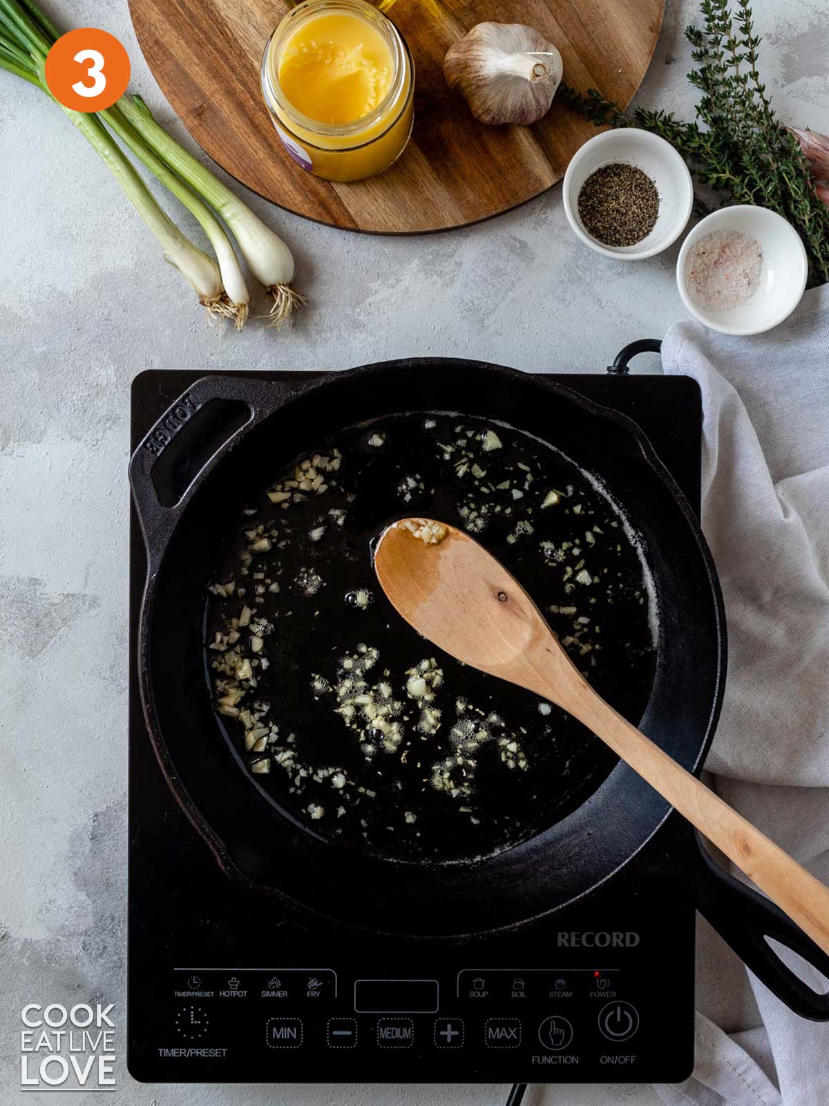 Garlic cooking in a skillet with a wooden spoon.