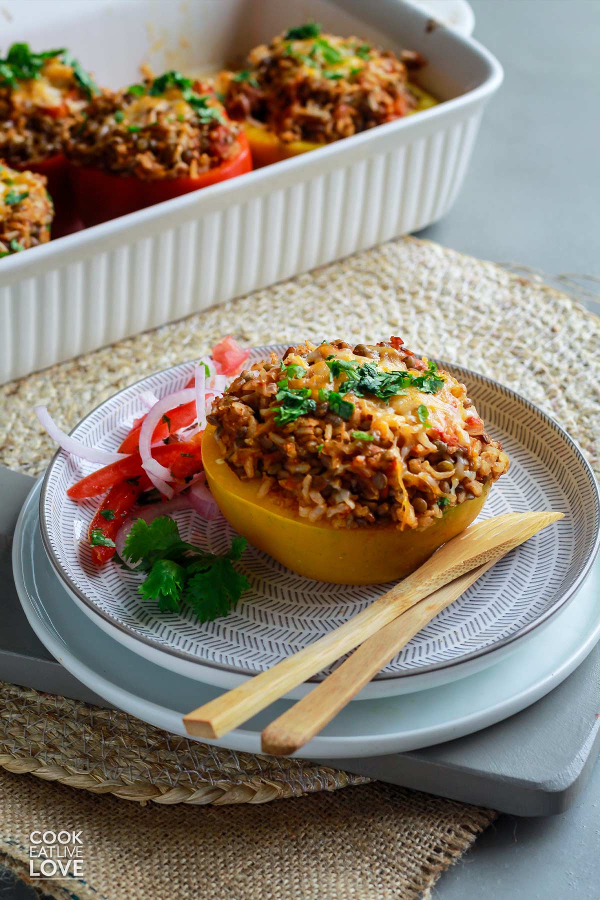 Brown rice and lentil stuffed peppers on a plate with a fork and knife.