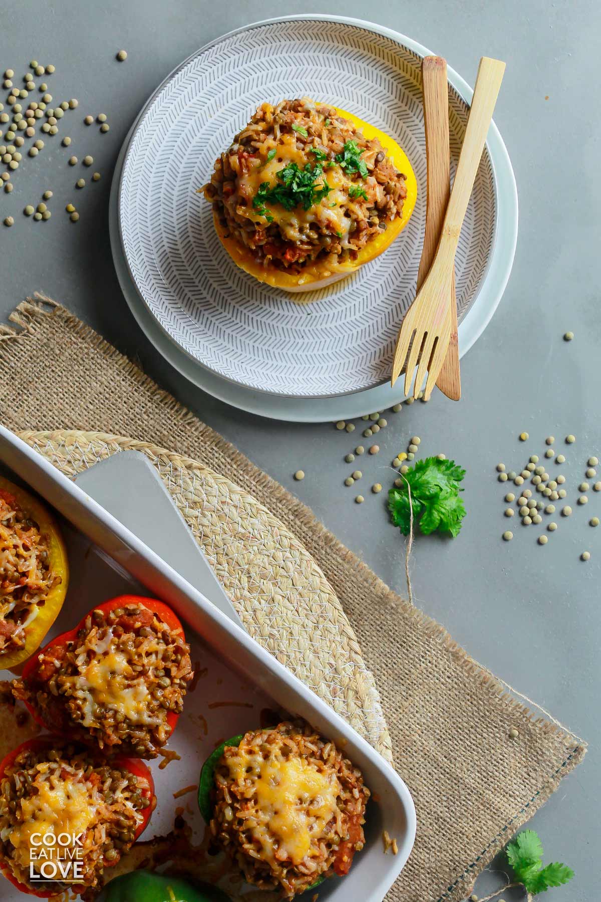 Lentil stuffed bell peppers in a casserole dish in the corner and one on a plate in the top middle.