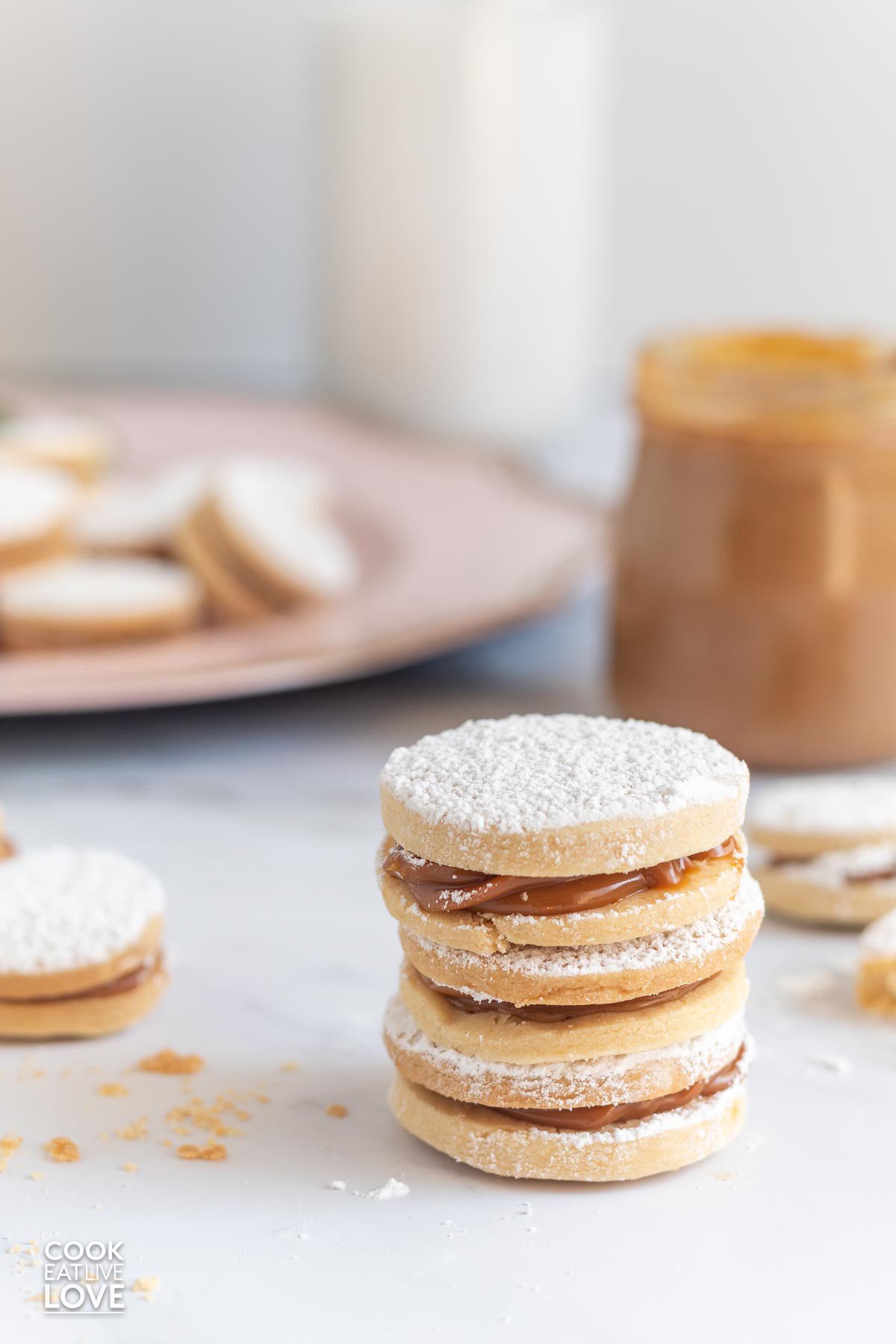 Stack of three alfajores on the counter with a jar of manjar blanco and cookies in the background.