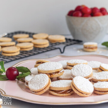 Peruvian alfajores cookies on a platter on the table with bowl of fruit and cookies on a cooling rack in the background.