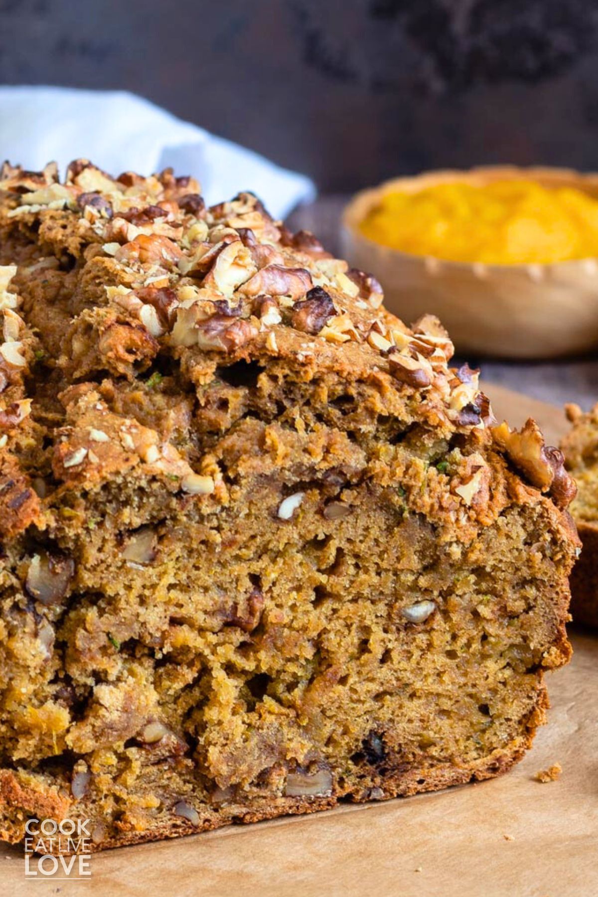 Pumpkin and zucchini bred with a slice cut to show inside and a small bowl of pumpkin in the background.