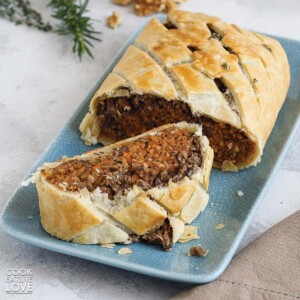 Vegan wellington with mushrooms and lentils on a platter with a slice cut and laying in front.