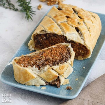 Vegan wellington with mushrooms and lentils on a platter with a slice cut and laying in front.
