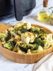 Bowl of broccoli and cauliflower in front of an air fryer.
