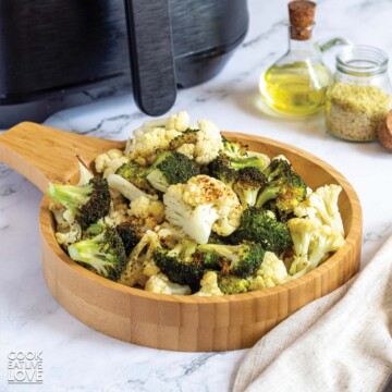 Bowl of broccoli and cauliflower in front of an air fryer.