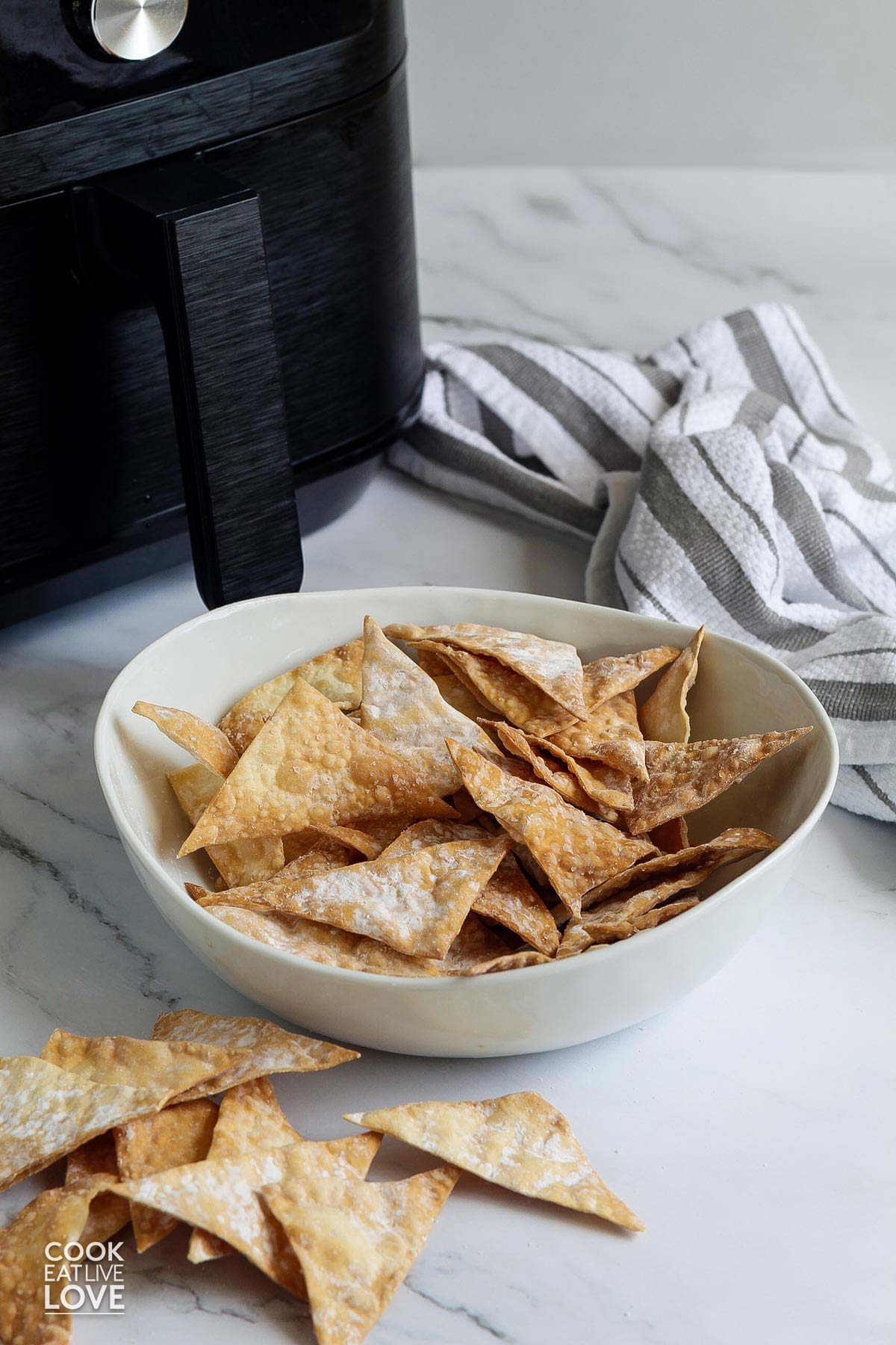 Bowl of air fryer wonton chips sitting in front of an air fryer.