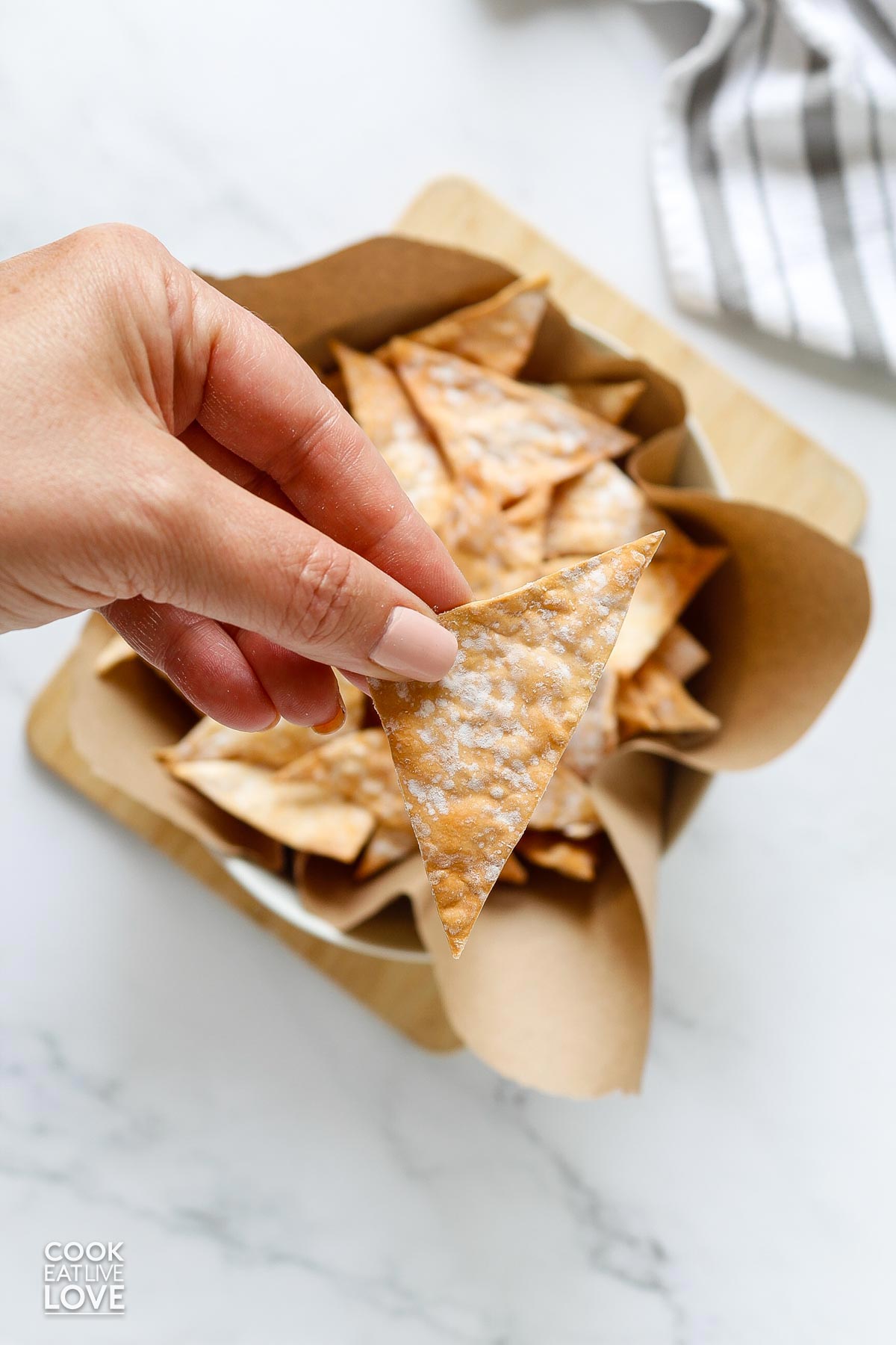 A hand picking up a crispy wonton chip from a basket.