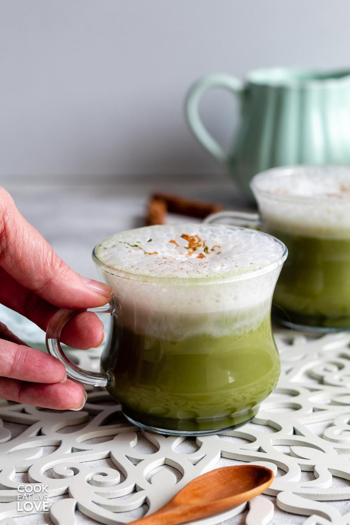 A hand reaching in to grab the handle of a mug of chai matcha latte.