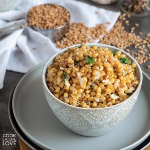 A bowl of cooked wheat berries in a bowl with dry wheat berry kernels in a measuring cup behind.