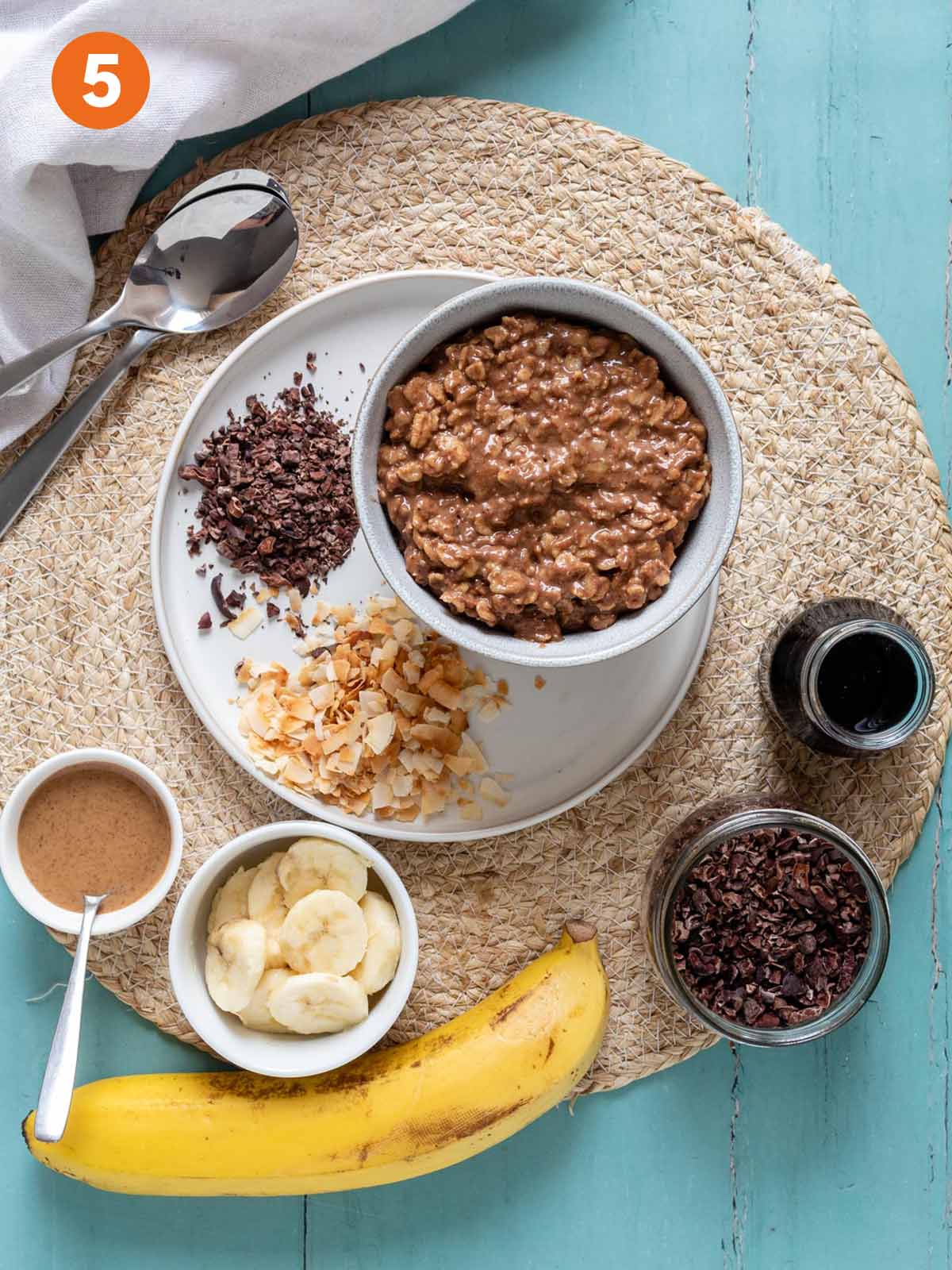 Chocolate oatmeal in a bowl on a plate surrounded by various toppings.