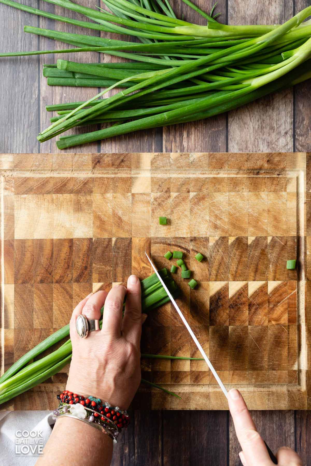 A hand holding the green onions and cutting into small straight pieces.