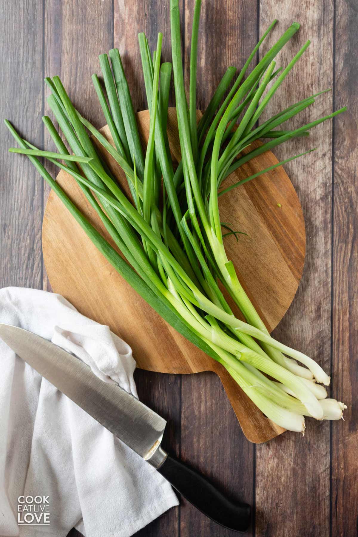 Green onions laying on a cutting board with a knife to the side.
