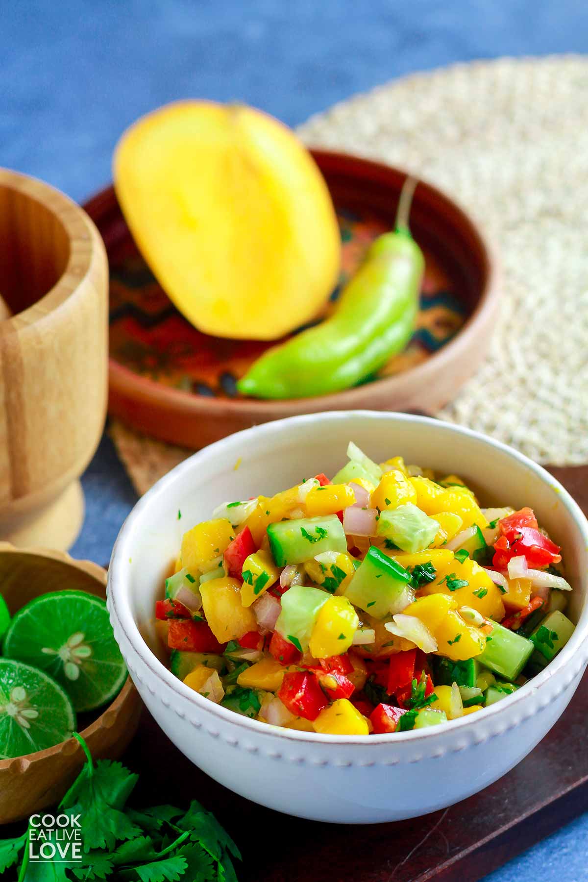 A bowl of mango salsa with a chile and mango half behind it.