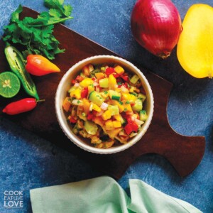 A bowl of 5 ingredient mango salsa on the table with fresh produce around it.