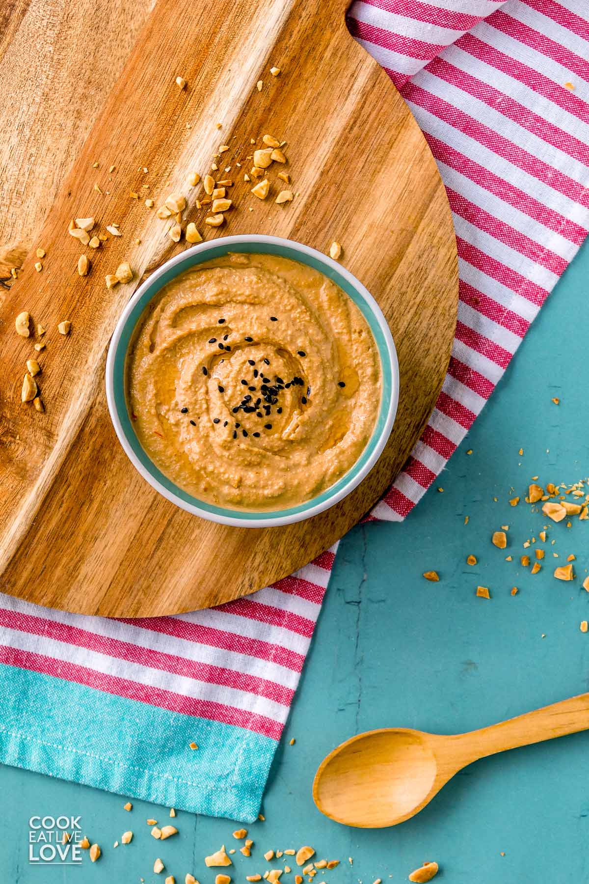 A bowl of peanut sauce on table on a round cutting board with a spoon to the side.