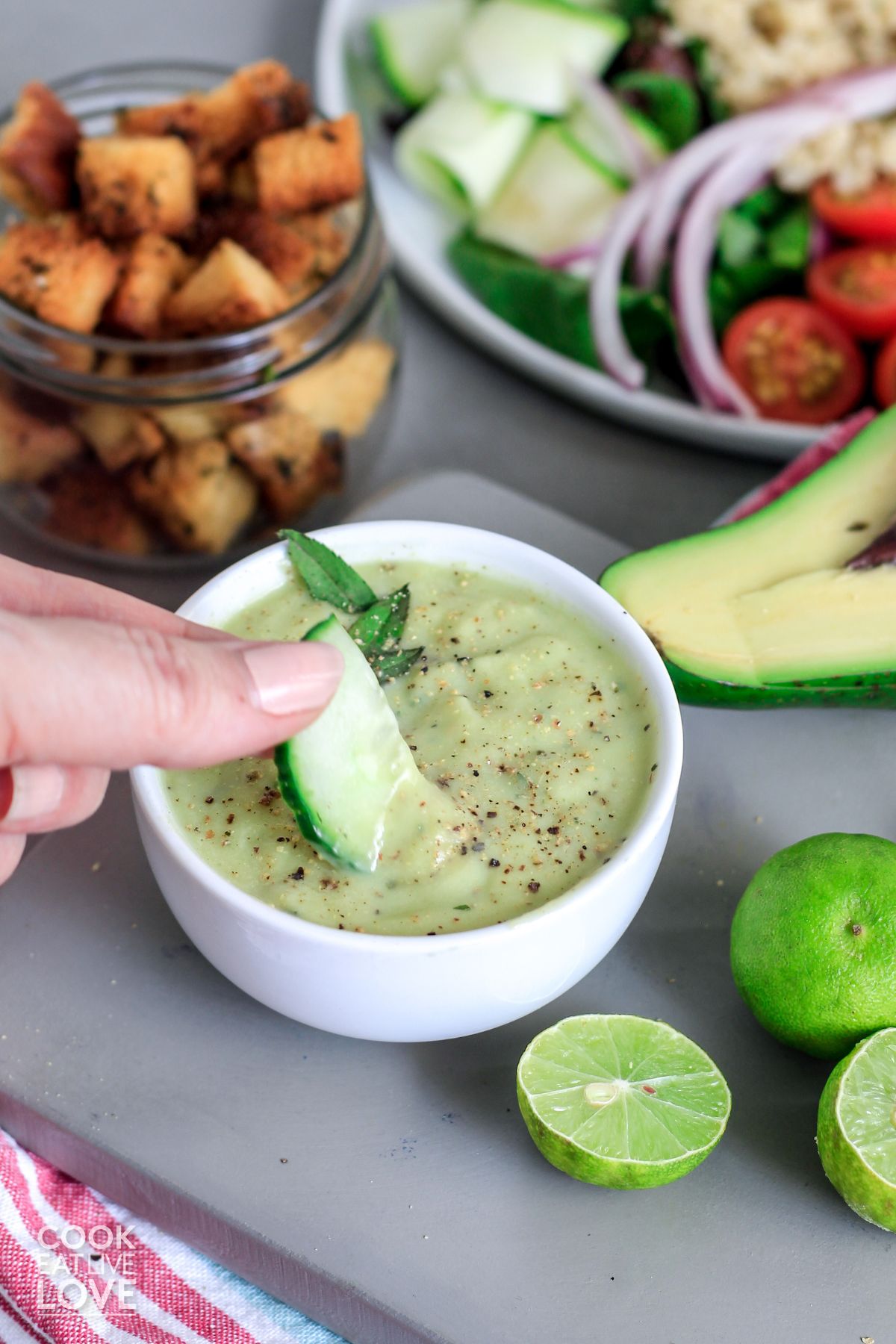 Avocado lime dressing served up in small white bowl with herb garnish and limes