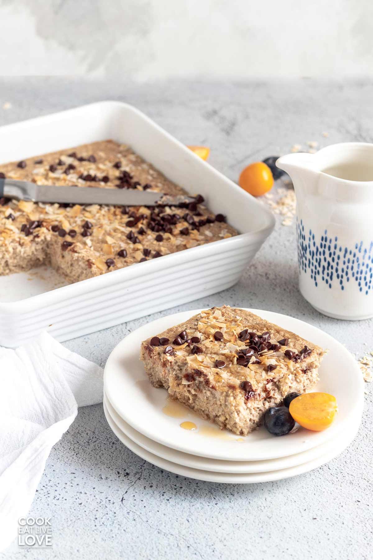 Baked oatmeal without bananas on a plate with fruit and a casserole dish in the background.