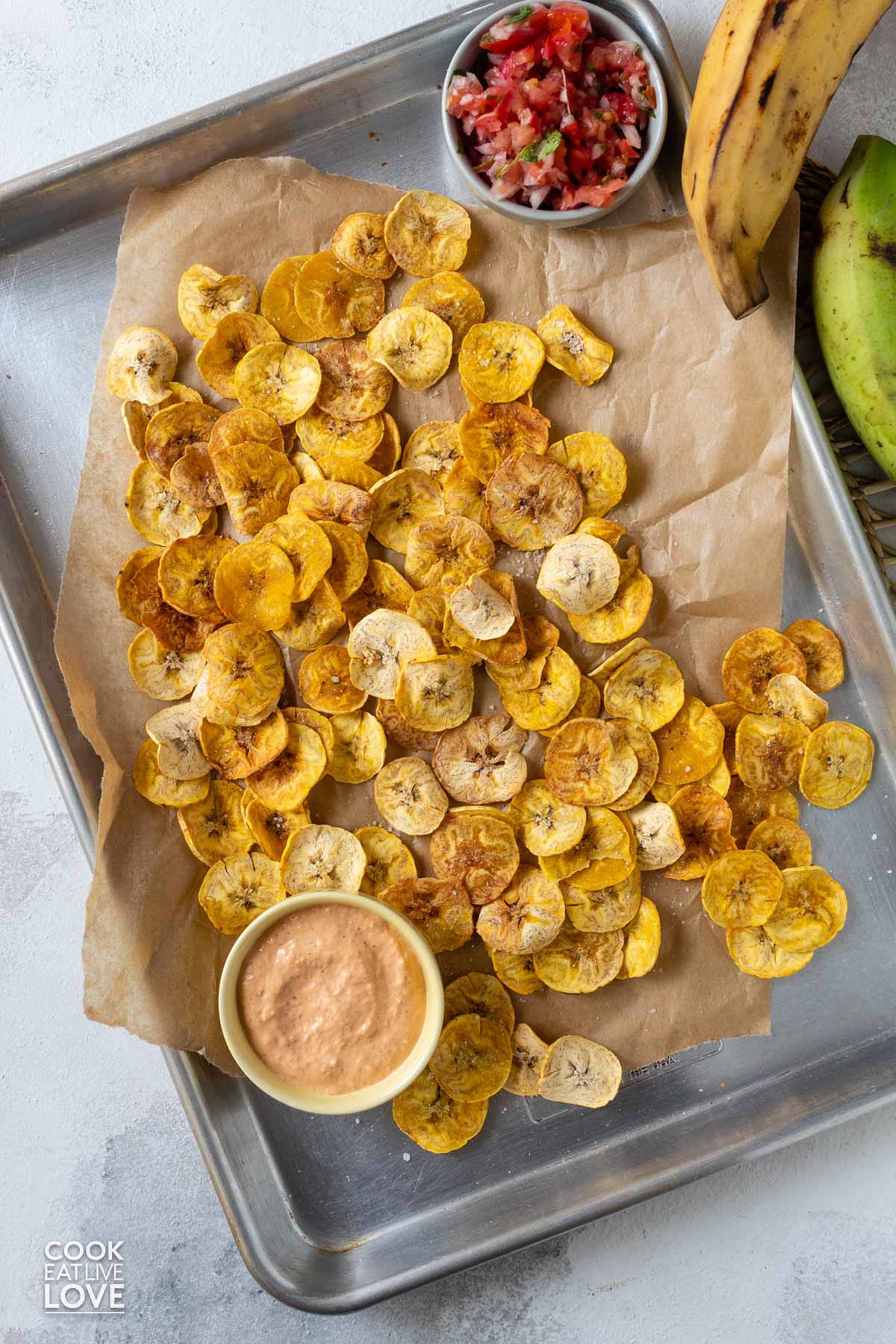Baked plantain chips on a parchment paper and baking tray with sauces.