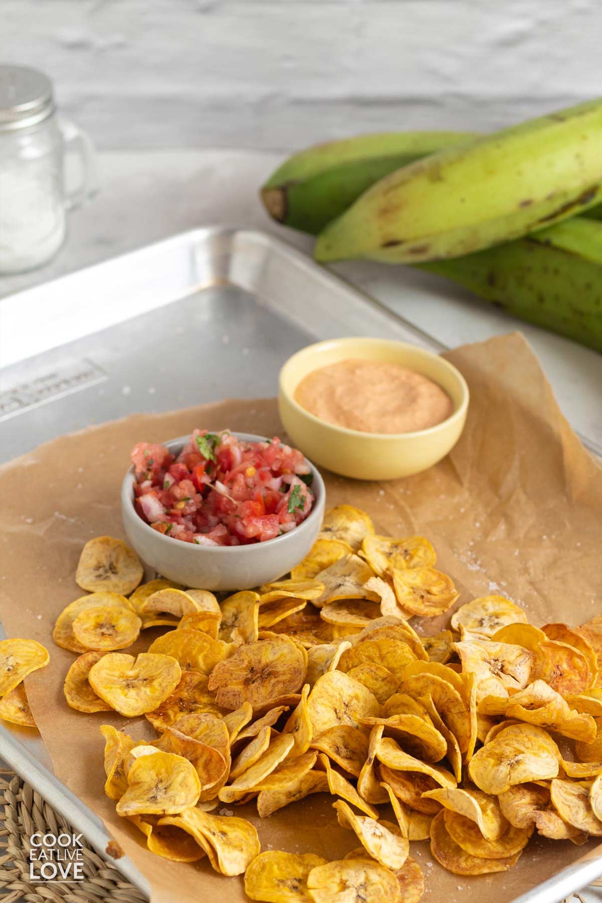 Paleo plantain chips on a baking tray with salsa and creamy sauce in the background.