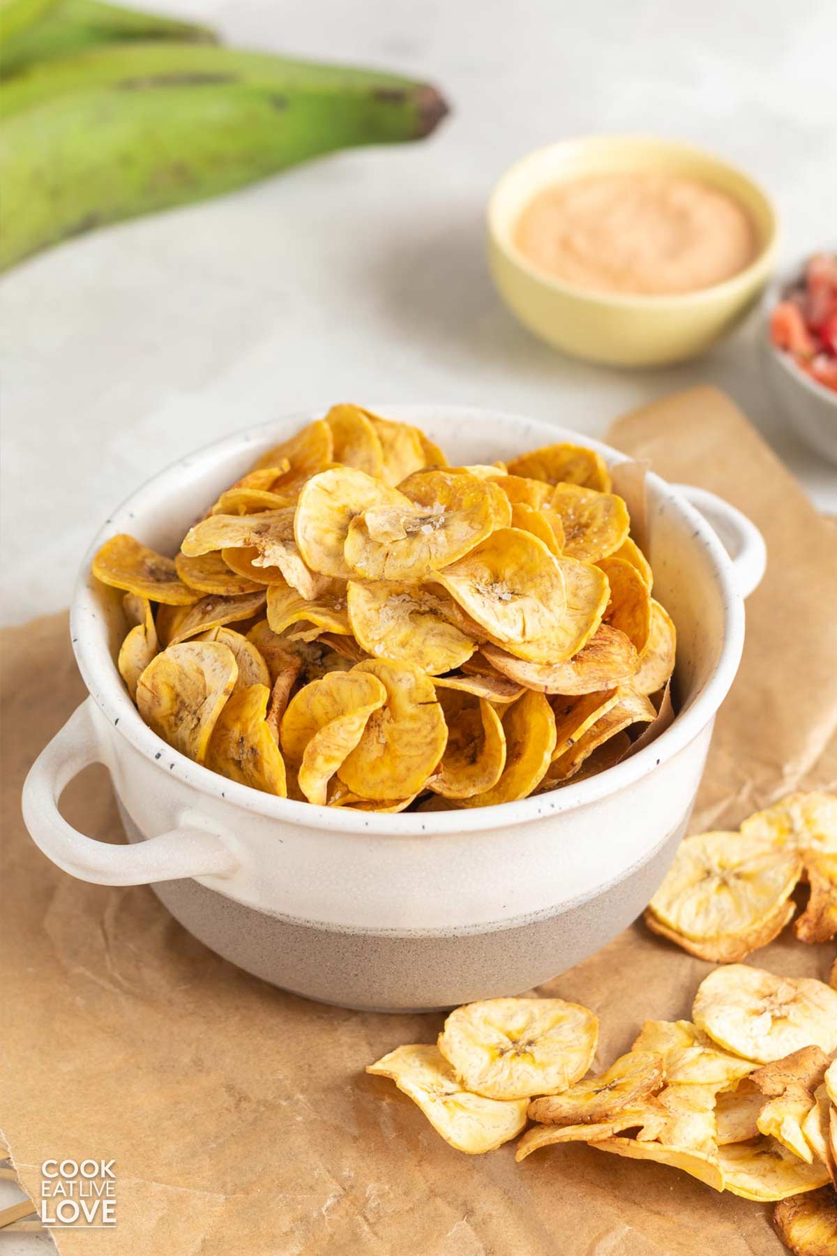 A bowl of baked plantain chips on a piece of parchment paper.