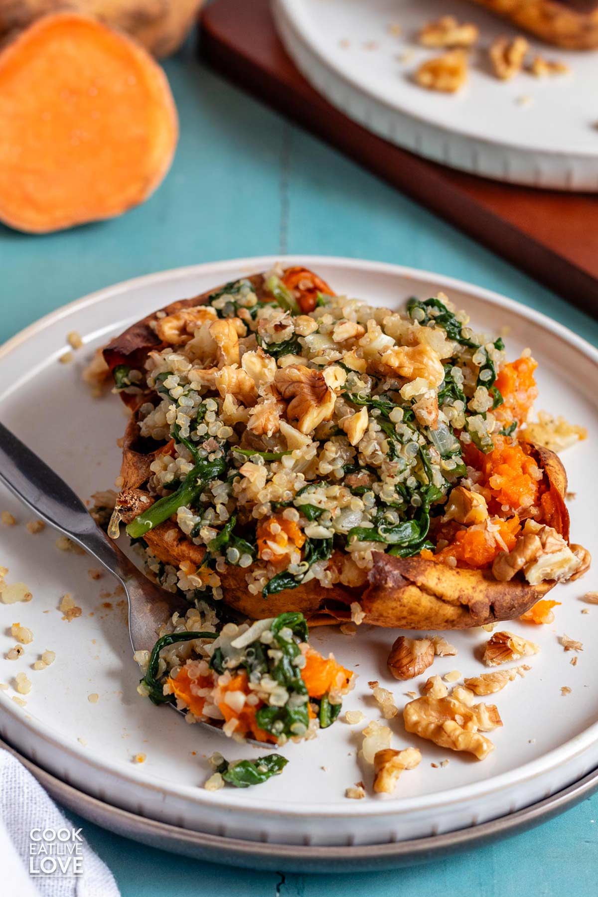 A baked stuffed sweet potato with quinoa and spinach served on a whtie plate.