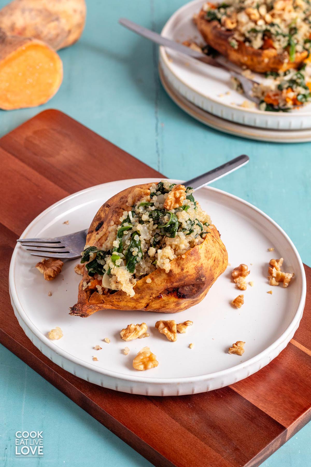 Baked stuffed sweet potato topped spinach, quinoa, and walnuts served on a white plate.