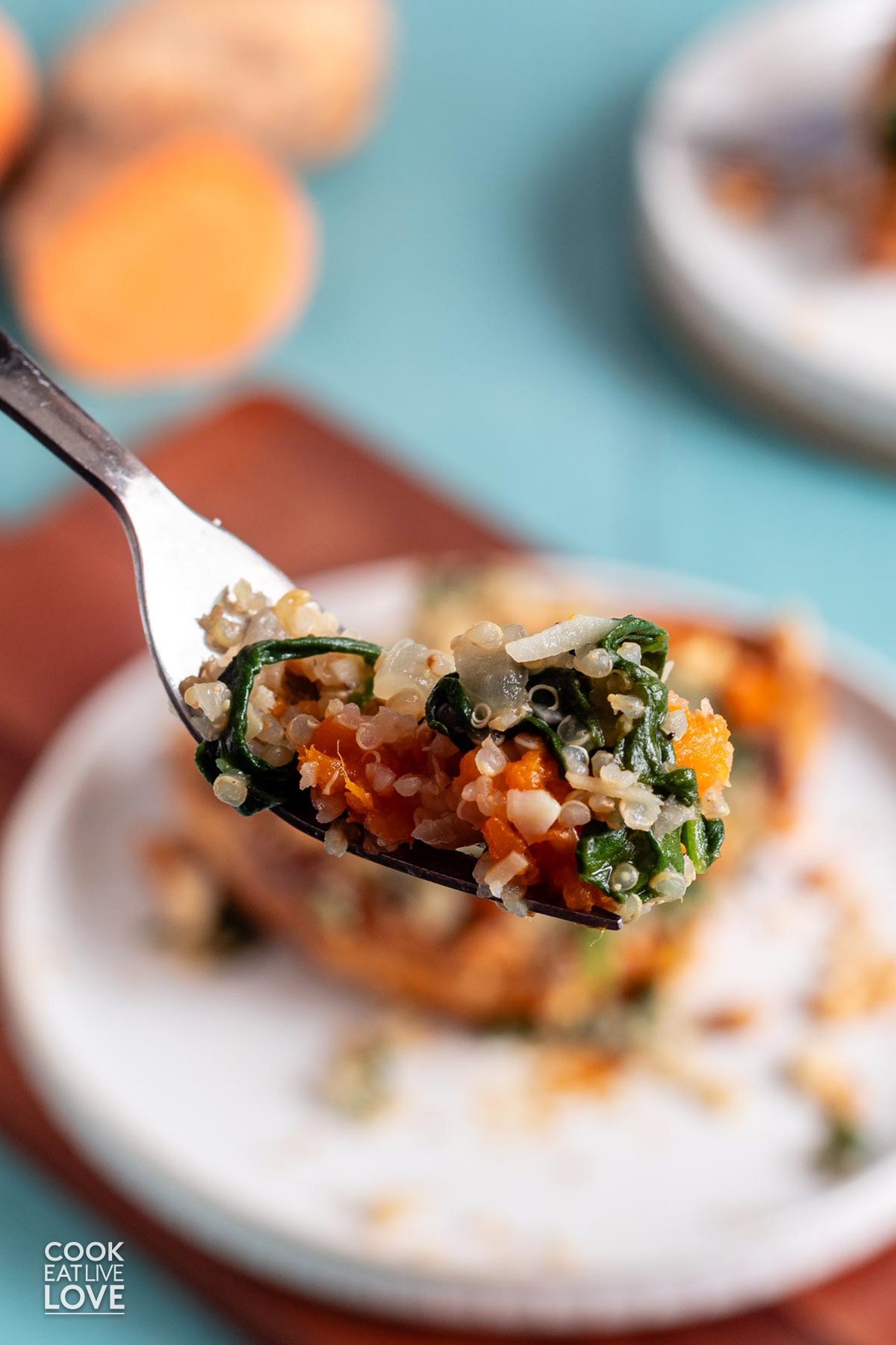 A forkful of sweet potato with quinoa and spinach held up over the plate.