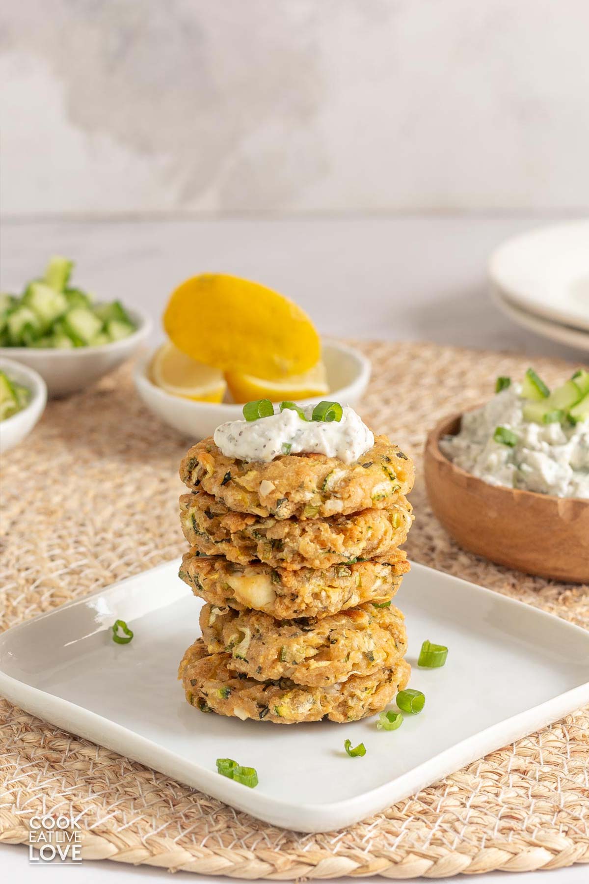 Stack of healthy zucchini fritters on a white plate with yogurt sauce on top.