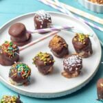 A plate of frozen banana bites on the table dipped in chocolate and topped with assorted sprinkles.