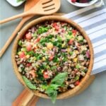Barley salad in a wooden bowl with wooden utensils to the side.