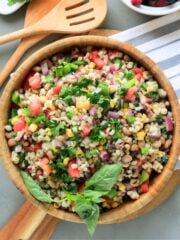 Barley salad in a wooden bowl with wooden utensils to the side.
